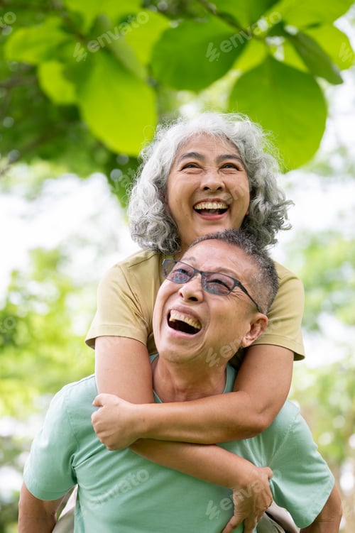 Preview: Glasses old man carrying woman on his back and smiling together while standing or walking in park.