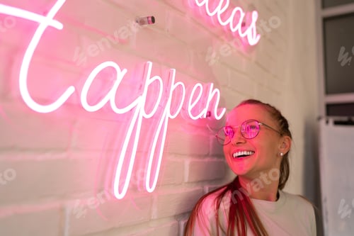 Preview: excited female millennial in spectacles reading colorful neon text and smiling