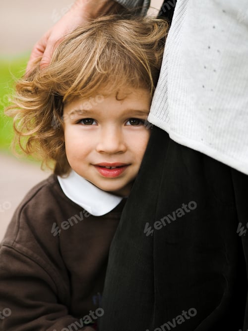 Preview: Cute curly child hug his mother’s leg on a street.