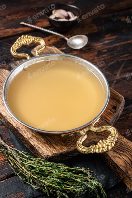 Preview: Clear broth stock without meat in cooking skillet. Wooden background. Top view