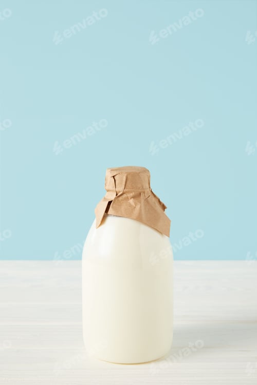 Preview: closeup view of fresh milk in bottle wrapped by paper on blue background
