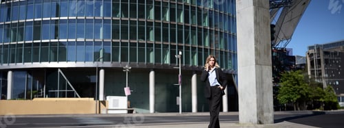 Preview: Young corporate woman in suit walking on street and talking on mobile phone. Businesswoman having