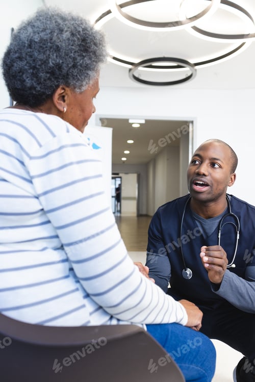 Preview: African american male doctor talking with senior woman in hospital waiting room