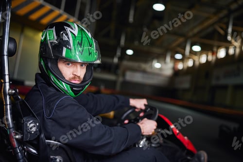 Preview: portrait of man in helmet and sportswear driving go kart on indoor circuit, adrenaline concept