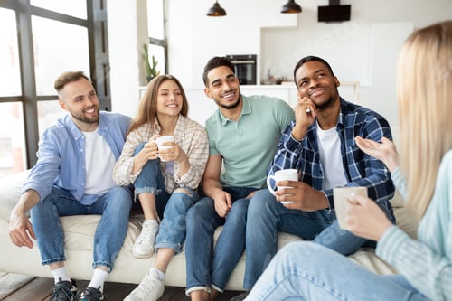 Preview: Multiethnic young friends enjoying conversation, drinking tea or coffee at home