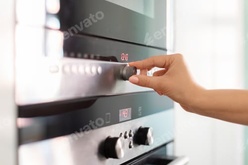 Preview: Female hand adjusting temperature on electric oven while cooking in kitchen