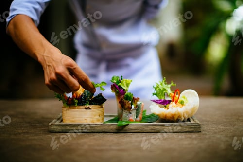 Preview: Close up of chef putting the final touches on a dish of salads and spring rolls.