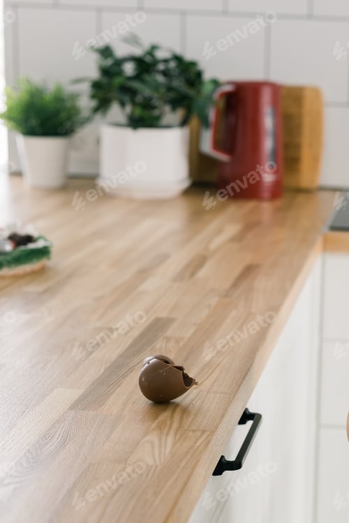 Preview: Broken chocolate egg on wooden table in kitchen - vertical photo with copy space and empty place for