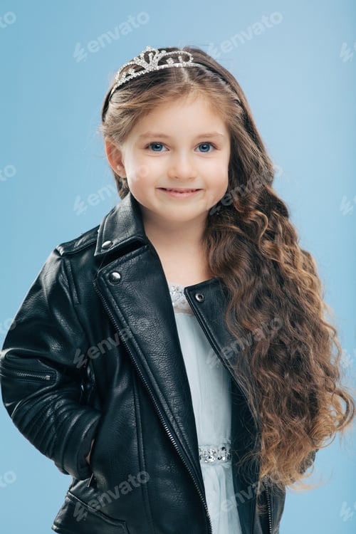 Preview: attractive small female child has long curly hair, wears crown and leather jacket smiles positively