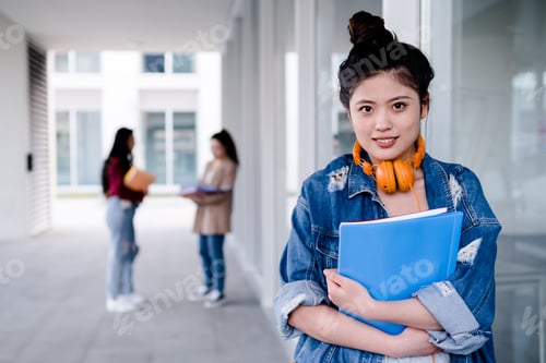Preview: Asian university student looking at the camera and holding folders while standing