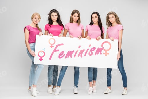 Preview: attractive girls holding large sign with feminism lettering on grey background