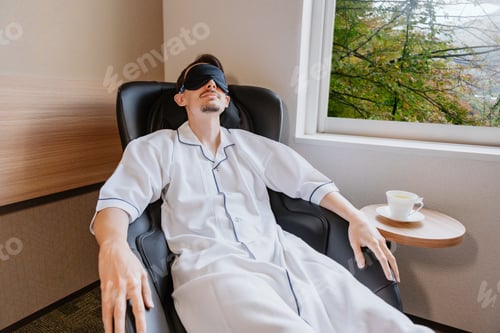Preview: Man wearing sleep mask relaxing in massage chair indoors, resting and reclining during spa session