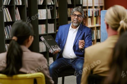 Preview: Middle Aged Man Presenting Book to Diverse Adult Audience in Library