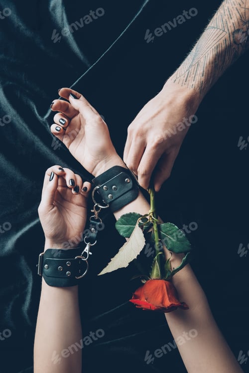 Preview: cropped shot of woman in black leather handcuffs and man holding red rose flower
