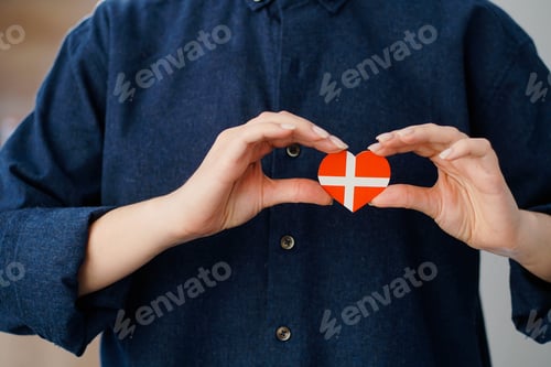Preview: Young woman holding a heart in the form of a flag of Denmark.