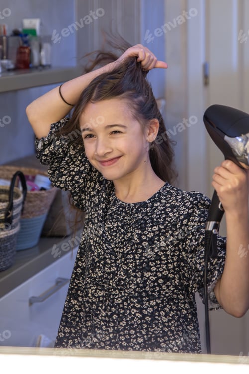 Preview: A girl dries her hair with a hairdryer in the bathroom. Hygiene concept.
