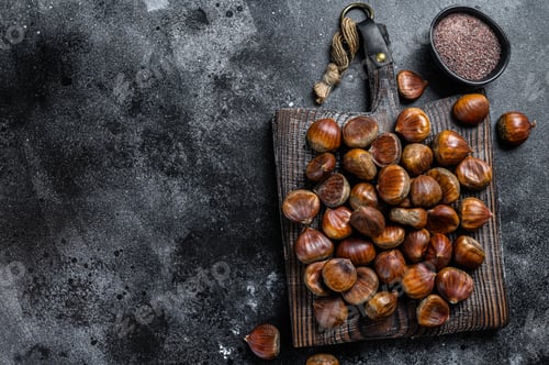 Preview: Raw chestnuts on a wooden cutting board. Black background. Top view. Copy space