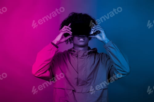 Preview: Young African male with VR glasses standing under the blue and purple lights