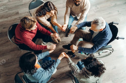 Preview: Diverse group of people holding hands in circle during therapy session