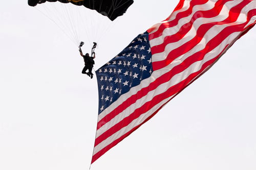Preview: Scenic view of the American flag and a guy parachuting in the clear sky background