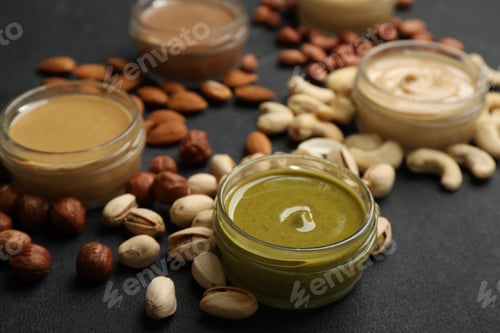 Preview: Jars with butters made of different nuts and ingredients on black table, closeup