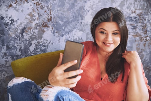 Preview: Smiling Woman Relaxing in Armchair Using Smartphone