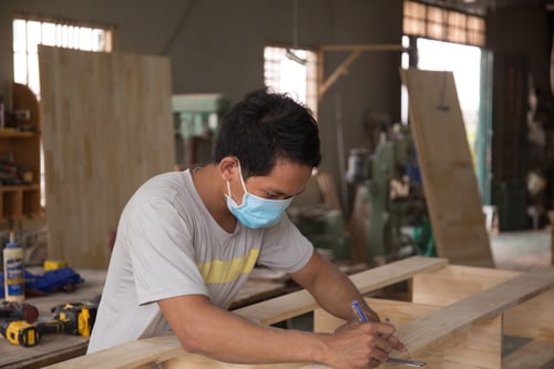 Shallow focus of a Southeast Asian carpenter working on polished wood planks in the workshop