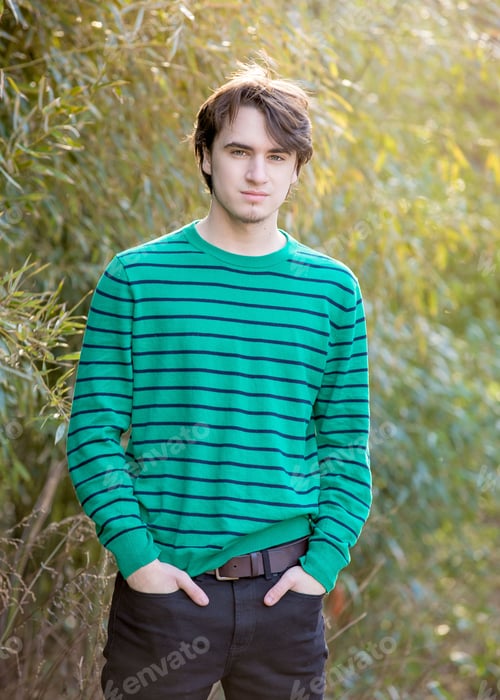 Preview: Handsome young man wearing green striped sweater standing with hands in pockets in front of bamboo