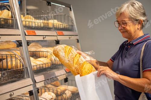 Preview: Elderly woman buying a rustic bakery bread at the supermarket by putting it in a paper bag