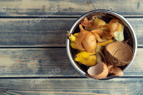 Preview: Metal bowl full of organic food scraps and peel rubbish on wooden background. Compost and manure