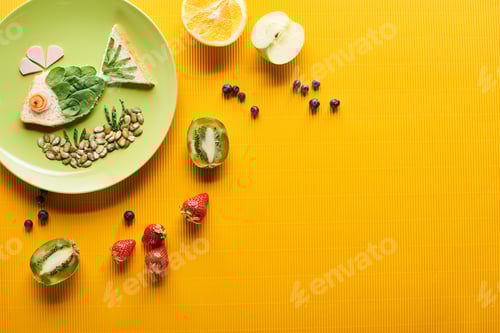 Preview: top view of plate with fancy fish made of food near scattered fruits on colorful orange background