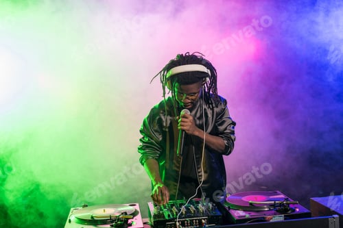 Preview: professional african american DJ in headphones with sound mixer in nightclub