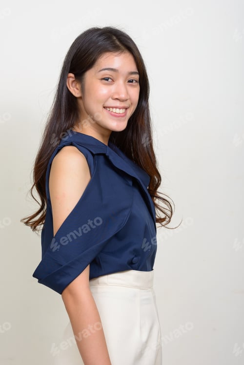 Preview: Profile view of happy young beautiful Asian businesswoman looking at camera