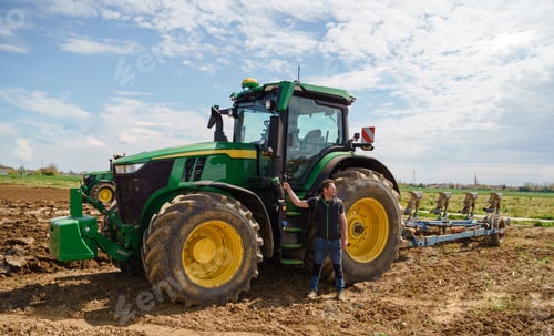 Preview: A skilled farmer proudly stands next to his plowing tractor, demonstrating his expertise in field