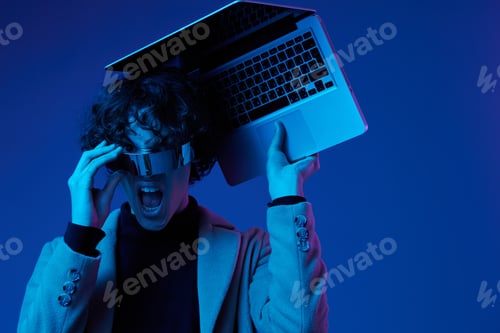Preview: Portrait of a stylish male hacker with a laptop and futuristic glasses in blue light, cyber security