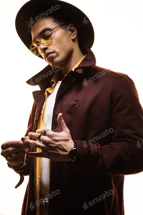 Preview: fashionable mixed race man in hat and sunglasses putting on rings isolated on white