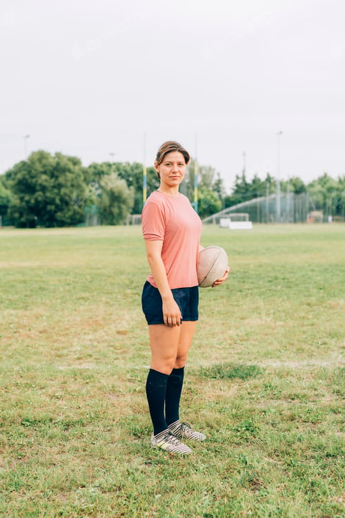 Preview: Confident sportswoman posing with a rugby ball on the field.