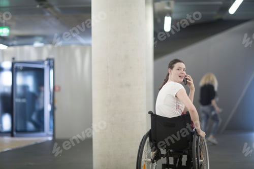 Preview: Young woman using wheelchair in underground parking lot talking on smartphone
