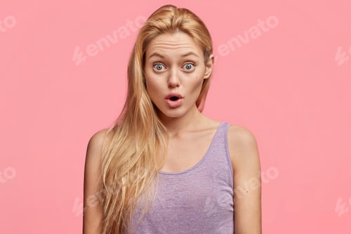 Preview: Shocked blonde blue eyed young female keeps jaw dropped, finds out bad news about friend, stares at