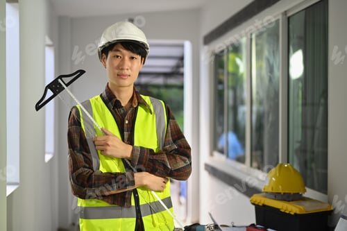 Preview: Portrait of asian man worker in safety helmet and reflective vest standing in construction site