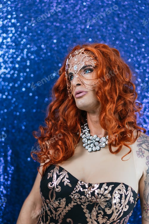 Preview: Confident drag queen in stylish mask and clothes while posing over a glitter background.