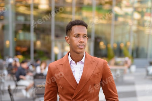 Preview: Portrait of handsome black African businessman outdoors in city thinking