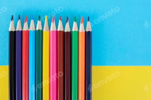 Preview: Bright colored pencils on yellow and blue paper background.
