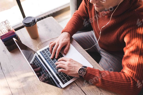 Preview: cropped view of man listening music in earphones and using laptop in cafe