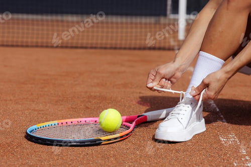 Preview: Tennis preparation tying shoelaces with racket and ball on clay court