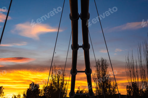 Preview: Sunset in a Mediterranean city with the silhouette of the metal structure of a suspended bridge.