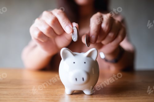 Preview: Closeup image of a woman putting coins into piggy bank for saving money concept