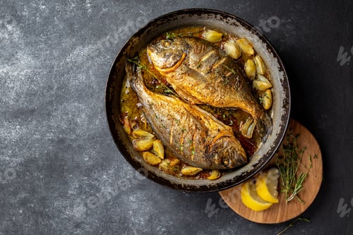 Preview: Baked sea bream or dorada with onion and herbs in pan on dark background