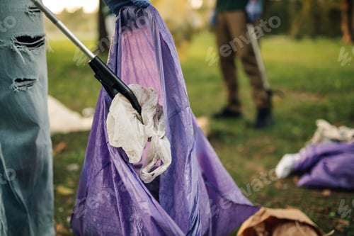 Preview: Volunteer picking up trash with grabber tool in public park