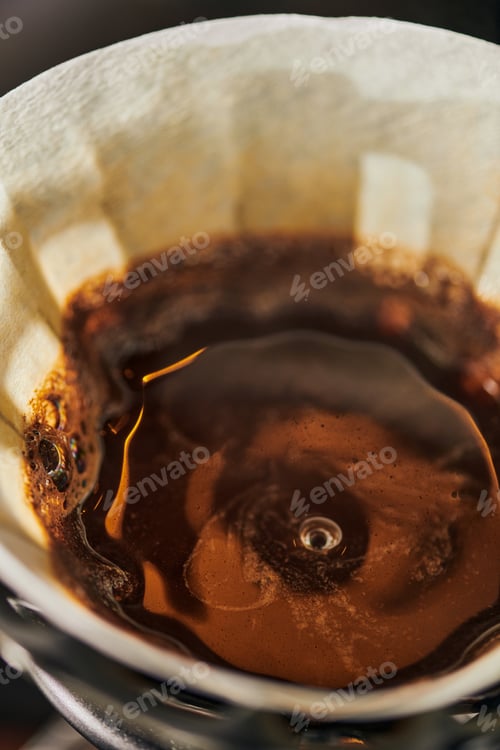 Preview: close up view of black, freshly brewed V-60 style espresso coffee with foam in paper filter bag